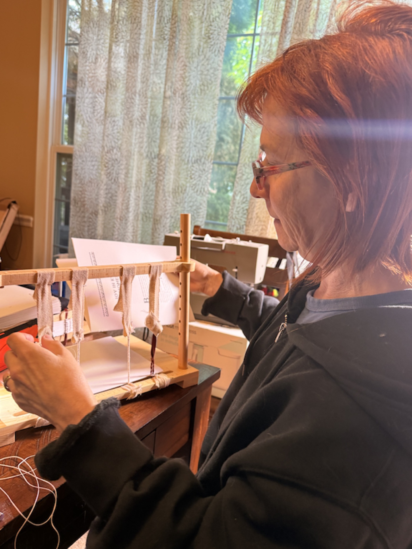 Debbi sewing a hand-bound magical record on a traditional bookbinding frame