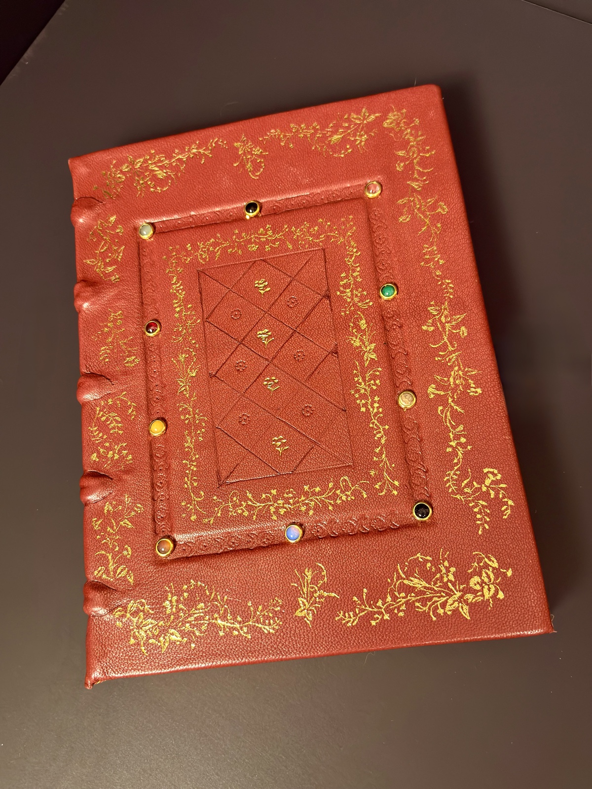Finished front cover at an angle — gold tooling and cabochon stones across the Ruby Red goatskin board