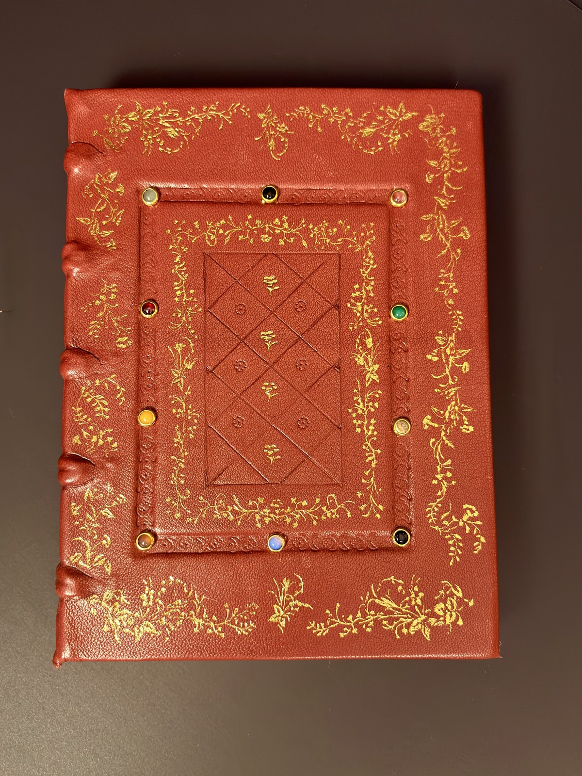 Finished front cover — gold-tooled foliate border framing twelve gold-bezel cabochon stones on Ruby Red Alran goatskin