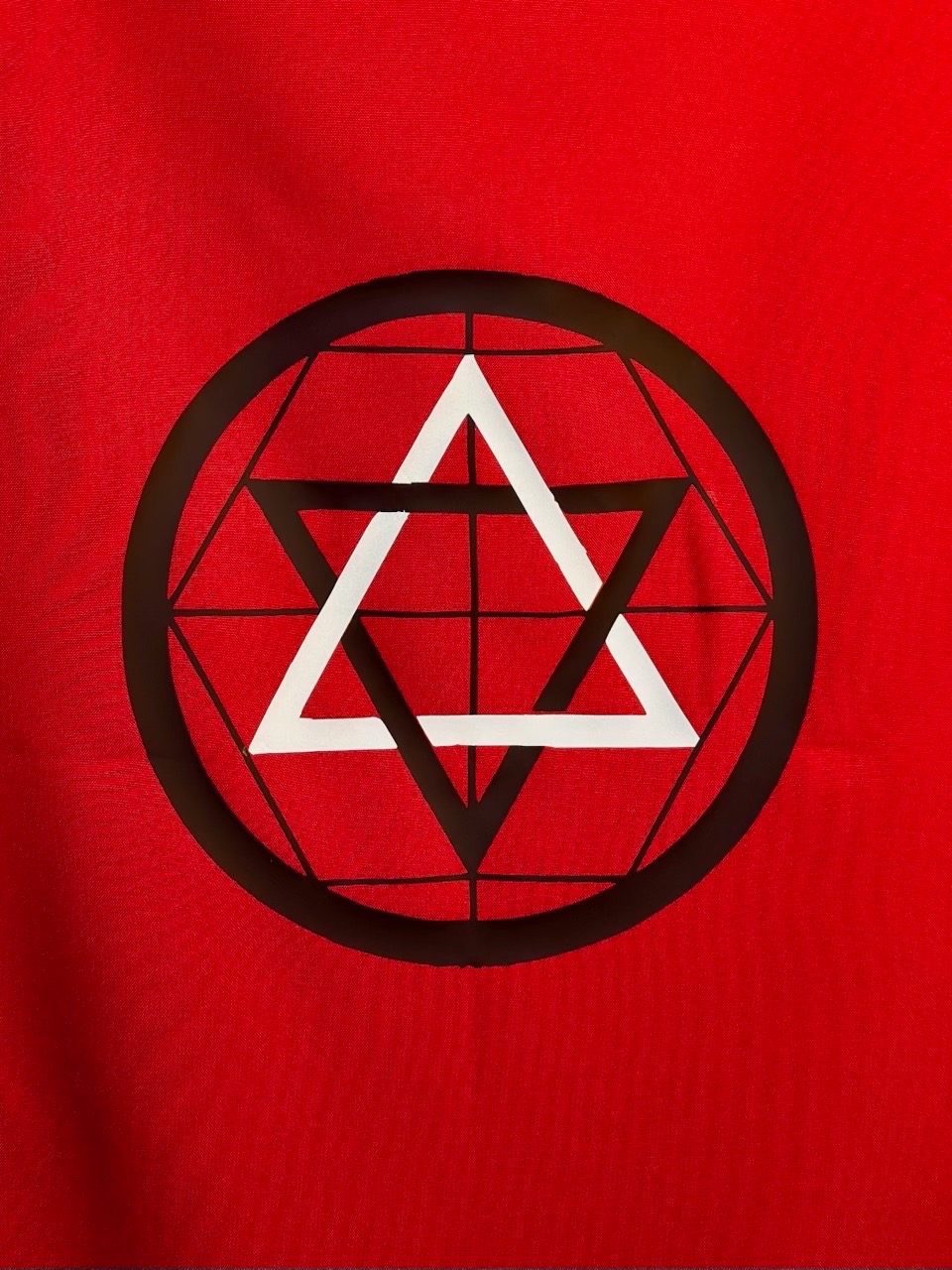 Martinist Banner emblem detail — interlocking black and white triangles within a black geometric circle on the deep red field